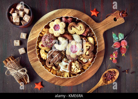 Piastra di biscotti di Natale su una tavola di legno scuro su sfondo rustico con decorazioni e ingredienti intorno Foto Stock