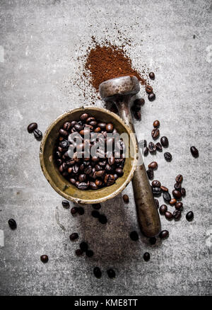 Chicchi di caffè tostati in un mortaio con pestello. su un sfondo di pietra. Foto Stock