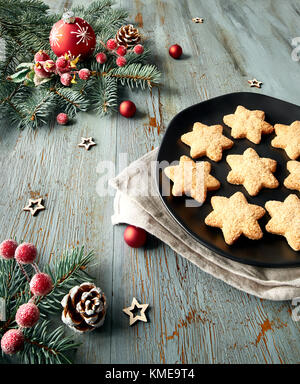 Rustico sfondo di Natale in verde e rosso a forma di stella i cookie su piastra nera con decorazioni di Natale. Foto Stock