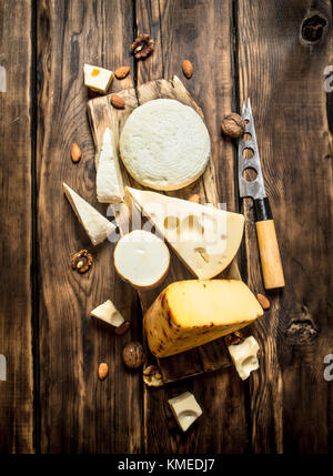 Pezzi di formaggio con i dadi su una scheda con un coltello su un tavolo di legno. Foto Stock