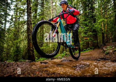 Woman mountain biker corse in discesa nel bosco su ghiaccio il sentiero dei laghi, STATI UNITI D'AMERICA Foto Stock