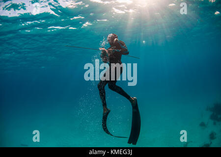 Tuffati dalla superficie dopo aver spiearato il pesce di mare mentre pesca all'angua in oceano, Clarence Town, Long Island, Bahamas Foto Stock