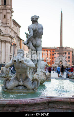 Turisti e gente del posto hanno trascorso una calda serata estiva bevendo vino e guardando la gente vicino alle numerose fontane in Piazza Navona, Roma. Foto Stock