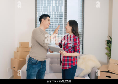 Concetto coppia giovane casa in movimento. Bella coppia Giovane dando alta cinque e sorridere mentre piedi tra lo spostamento di scatole di cartone Foto Stock