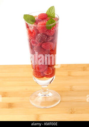 Bicchiere d'acqua pieno con lamponi isolati su tavola in legno Foto Stock