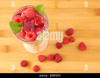 Bicchiere d'acqua pieno con lamponi isolati su tavola in legno Foto Stock