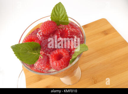 Bicchiere d'acqua pieno con lamponi isolati su tavola in legno Foto Stock