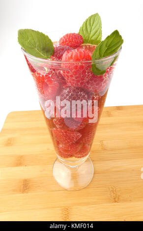 Bicchiere d'acqua pieno con lamponi isolati su tavola in legno Foto Stock