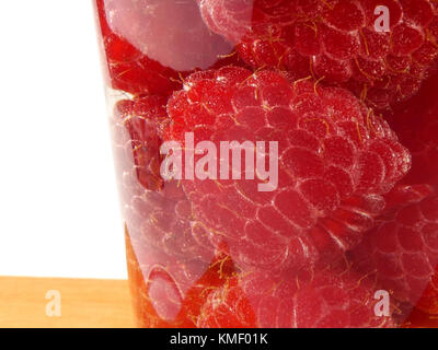 Bicchiere d'acqua pieno con lamponi isolati su tavola in legno Foto Stock