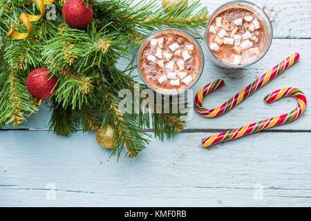 Due bicchieri di cacao con marshmallows e albero di Natale con i giocattoli in legno bianco sullo sfondo. Foto Stock