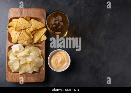 Birra in bicchieri primo piano sul tavolo in cemento. Birra e spuntini sono patatine e nachos in ciotola di legno con souce di formaggio. Vista dall'alto. Spazio di copia. Bere e. Foto Stock