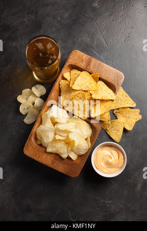 Birra in bicchieri primo piano sul tavolo in cemento. Birra e spuntini sono patatine e nachos con vista dall'alto del souce di formaggio. Spazio di copia. Drink e snack per il fo Foto Stock