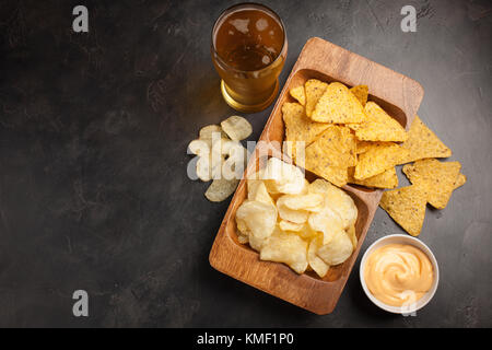 Birra in bicchieri primo piano sul tavolo in cemento. Birra e spuntini sono patatine e nachos in ciotola di legno con souce di formaggio. Vista dall'alto. Spazio di copia. Bere e. Foto Stock