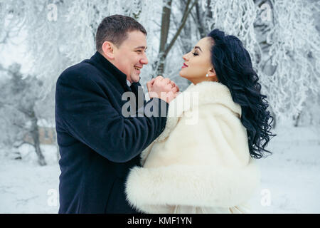 Sensibile ritratto della allegro bella sposa giovane. lo sposo è il riscaldamento delle mani del suo affascinante bruna sposa nella foresta d'inverno. Foto Stock