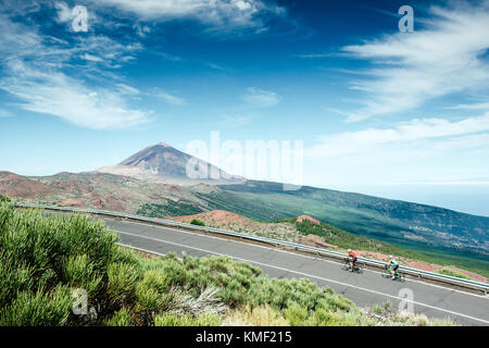 Due ciclisti a pedalare su strada di montagna con il monte Teide sullo sfondo,il Parco Nazionale Teide,Tenerife,Isole Canarie,Spagna Foto Stock