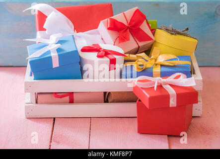 Gifting Tema immagine con un mazzetto di colorfully avvolto presenta in un bianco cratere di legno su una tabella di colore rosa e blu sullo sfondo di legno. Foto Stock