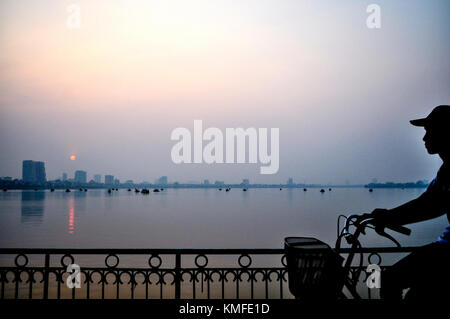 Un uomo su una bicicletta passando per il west lake - Hanoi, Vietnam Foto Stock