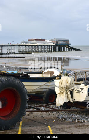 Cromer Pier in Norfolk con il granchio barche da pesca e il lancio di trattori sulla spiaggia sabbiosa in primo piano. I pescatori e la pesca in Norfolk a cromer Foto Stock