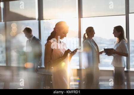 Imprenditrice texting con un telefono cellulare nella soleggiata sala conferenze Foto Stock