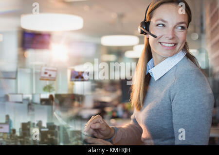 Imprenditrice sorridente con cuffia lavoro in ufficio Foto Stock