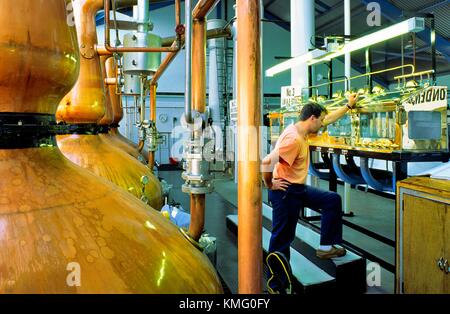 Laphroaig distilleria di whisky, isola di Islay, Scozia. Ancora uomo di controllo dei livelli nello spirito di sicuro accanto a pentola di rame di immagini fisse Foto Stock