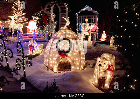 Outdoor decorazione di Natale di notte. Luci e ornamenti illuminati incandescente al buio, casa cortile coperto di neve. Foto Stock