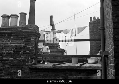 Slum Poverty Londra anni '1960 Regno Unito. Bambino britannico etnico di colore che gioca sul tetto piatto, usato dalla famiglia come area giochi all'aperto sulla terrazza. Baraccopoli vittoriani edoardiani terrazzati in fase di demolizione come parte di un programma di slum di Kilburn, North London. Notare il rubinetto dell'acqua esterna sopra il secchio di plastica (a destra della fotografia) Inghilterra 1967 1960s Regno Unito HOMER SYKES Foto Stock