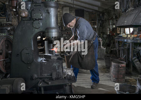 Fabbro martellando la barra di ferro calda rossa nella macchina del martello a. officina Foto Stock