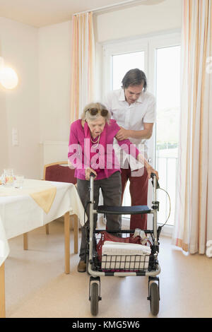 Donna anziana che aiuta la donna anziana che usa il camminatore su ruote Foto Stock