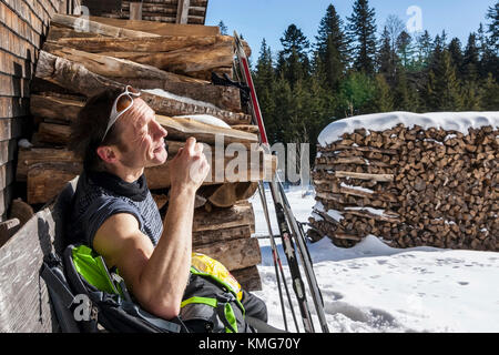 Uomo che si riposa sulla panchina di fronte a un tronco cabina Foto Stock