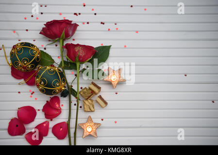 Christmas Romantic cibo fotografia immagine con rose rosse fiori candele accese e rosso verde ninnolo decorazione bianco su uno sfondo di legno con spazio di copia Foto Stock