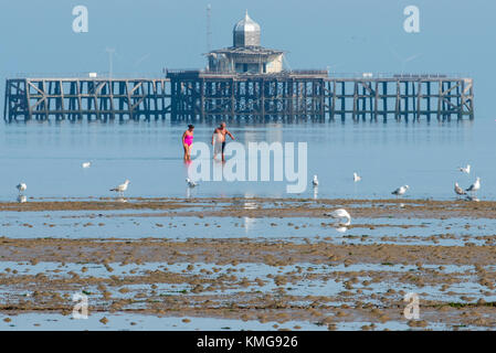 Un paio di indossare il costume da bagno passeggiate in mare Torna alla spiaggia dopo aver guardato le rovine del vecchio molo in Herne Bay, Kent. Foto Stock