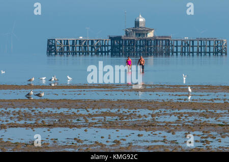 Un paio di indossare il costume da bagno passeggiate in mare Torna alla spiaggia dopo aver guardato le rovine del vecchio molo in Herne Bay, Kent. Foto Stock