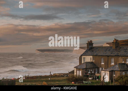 Birling Gap, East Sussex, Regno Unito 7 dicembre 2017..Sun si rompe tra le nuvole illuminando Seven Sisters falesie e cottage gesso come estremità meridionali di Storm Caroline frusta il surf. Foto Stock