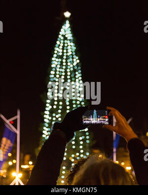 Trafalgar Square, Londra, 7 dicembre 2017. Una donna prende le foto dell'albero illumunato. La cerimonia annuale dell'illuminazione dell'albero di Natale di Trafalgar Square si svolge nella piazza, con turisti e londinesi che guardano l'interruttore ufficiale, oltre a canti e canti corali in un'atmosfera festosa. L'albero di Natale di Trafalgar Square viene raccolto e donato ogni anno alla popolazione britannica dalla città di Oslo, Norvegia, dal 1947, e il 2017 è il suo 70° anniversario. Foto Stock