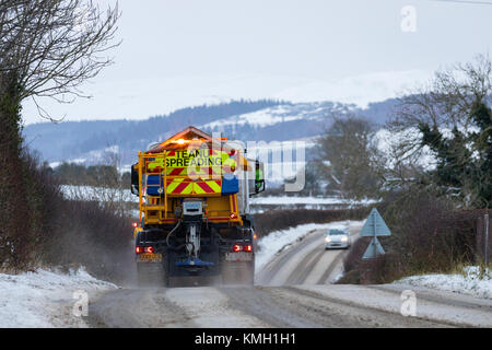 Flintshire, Galles, 9 dicembre 2017. Regno Unito Meteo. Con una Met Office avviso di colore giallo per la neve di oggi e di domani ambra che è una minaccia per la vita, Flintshire County Council spazzaneve e gritters si lotta per mantenere le strade per il prossimo 36ore. Un aratro di neve e gritter strade di compensazione nel rurale Flintshire villaggio di Lixwm con coperte di neve gamma Clwydian nella distanza © DGDImages/Alamy Live News Foto Stock