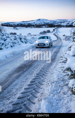 Flintshire, Nord, Regno Unito. Regno Unito Meteo. Con una Met Office avviso di colore giallo per condizioni di gelo per molti oggi. Pendolari si scia fino a un hard-neve e ghiaccio nero e di ciò che la stampa sta chiamando "Black Monday". Un driver di affrontare con cautela la neve ghiacciata coperto le strade rurali vicino al villaggio di Moel-y-Crio, Flintshire con la gamma Clwydian nella distanza Foto Stock