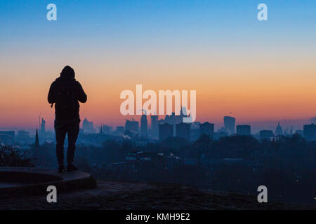 Londra, Regno Unito. 12 Dic, 2017. Londra, 12 dicembre 2017. Un inizio di mattina di walker attende il sorgere del sole su una chiara molto fredda mattina a Londra, visto da di Primrose Hill a Camden. Credito: Paolo Davey/Alamy Live News Foto Stock