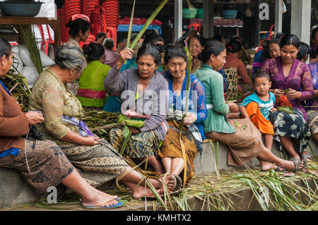 Donne nel villaggio di Tegalalang, che fanno cestini per portare offerte in un tradizionale rituale di cremazione comune, Tegalalang, Gianyar, Bali, indonesi Foto Stock