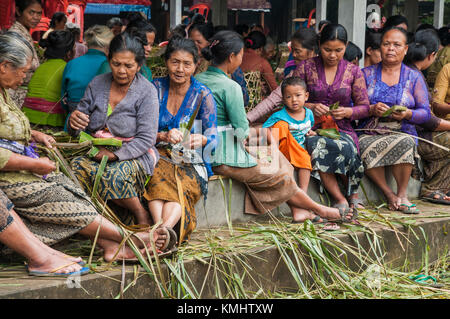 Donne nel villaggio di Tegalalang, che fanno cestini per portare offerte in un tradizionale rituale di cremazione comune, Tegalalang, Gianyar, Bali, indonesi Foto Stock