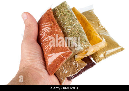 Varietà di spezie turche in confezione trasparente in mano sul bianco: origano, zafferano indiano, il cumino, il peperoncino, spice per insalata, coriandolo Foto Stock