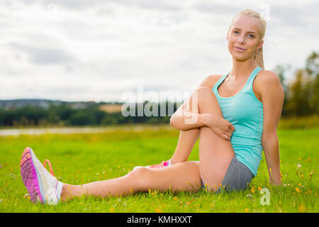 Montare donna bionda stretching all'aperto sull'erba Foto Stock