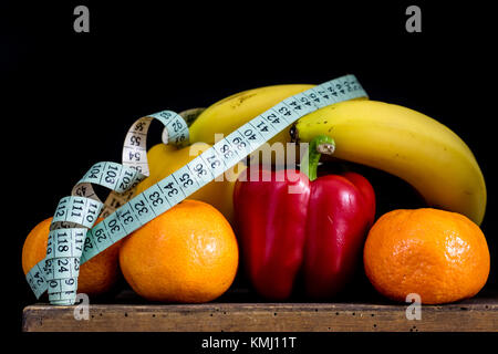 Gustosi frutti e verdure su un vecchio legno scuro tavolo da cucina. banana, peperoni e i mandarini sul tavolo di cucina insieme con la misura. black back Foto Stock