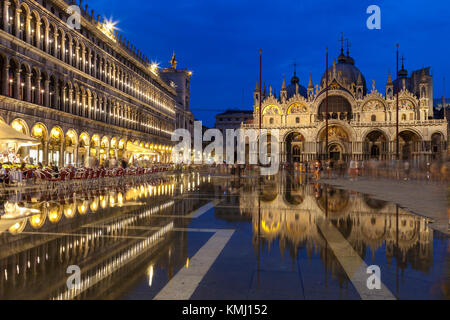 Basilica di San Marco si riflette in acqua alta in Piazza San Marco al crepuscolo durante ore blu , Venezia, Italia con motion blur su folle di turisti Foto Stock