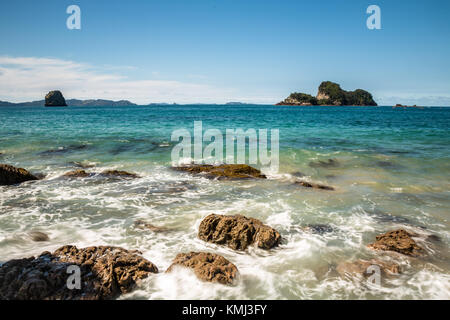 Onde dell'oceano pacifico break contro rocce frastagliate sul litorale di Nuova Zelanda. off shore oltre il blu-verdi acque dell'oceano pacifico stand Foto Stock