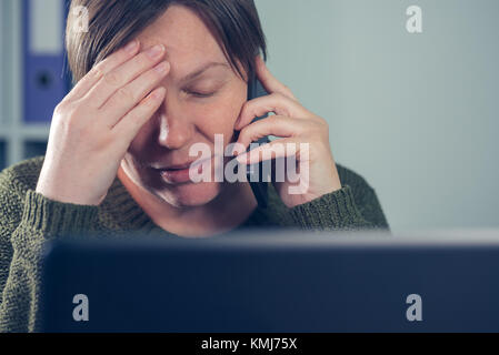 Stanco esausto freelancer femmina parlando al telefono mobile dalla sua propria start up business home office Foto Stock