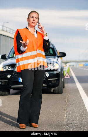 Donna sulla strada con ripartizione auto chiamando il traino di azienda Foto Stock