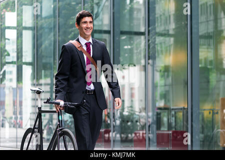 Felice active giovane uomo che indossa business suit mentre si cammina per il lavoro dopo gli spostamenti in bicicletta Foto Stock