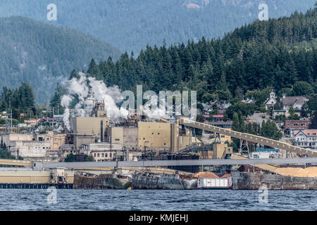 Gli scafi di cemento della seconda guerra mondiale formano un frangiflutti galleggiante di fronte al cartiera (ora chiuso) e alla storica Townsite nel fiume Powell, BC (2017). Foto Stock