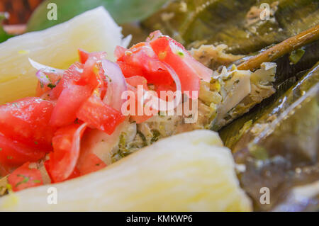 Close up di deliziosi piatti tipici alimenti amazonia, pesce cucinato in una foglia con yucca e piantaggine, con insalata di pomodoro e cipolle, servita in un piano in legno su un tavolo di legno Foto Stock